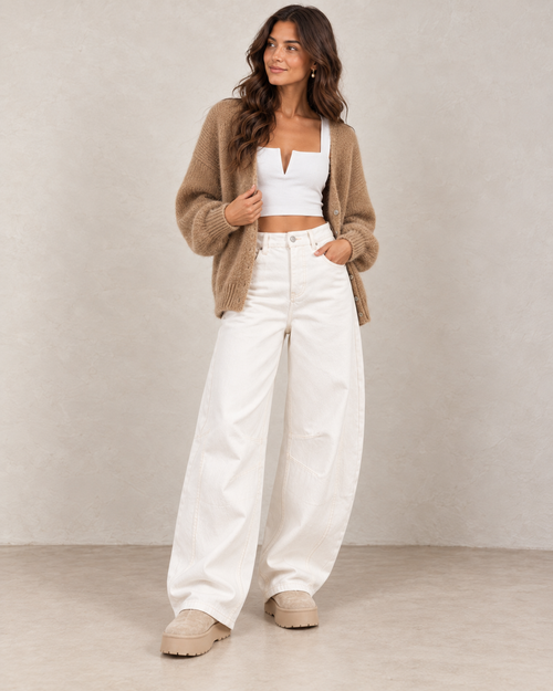 Bottines fourrées plateforme beige portées avec un jean barrel blanc, un top court blanc et un gilet camel