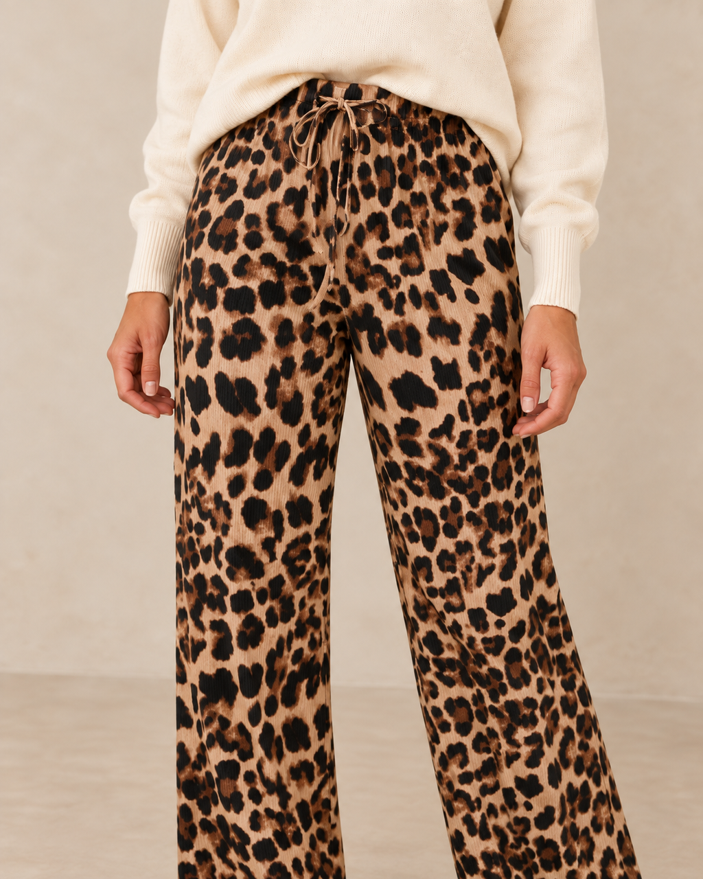 Gros plan du pantalon fluide léopard porté avec le pull écru sur fond beige