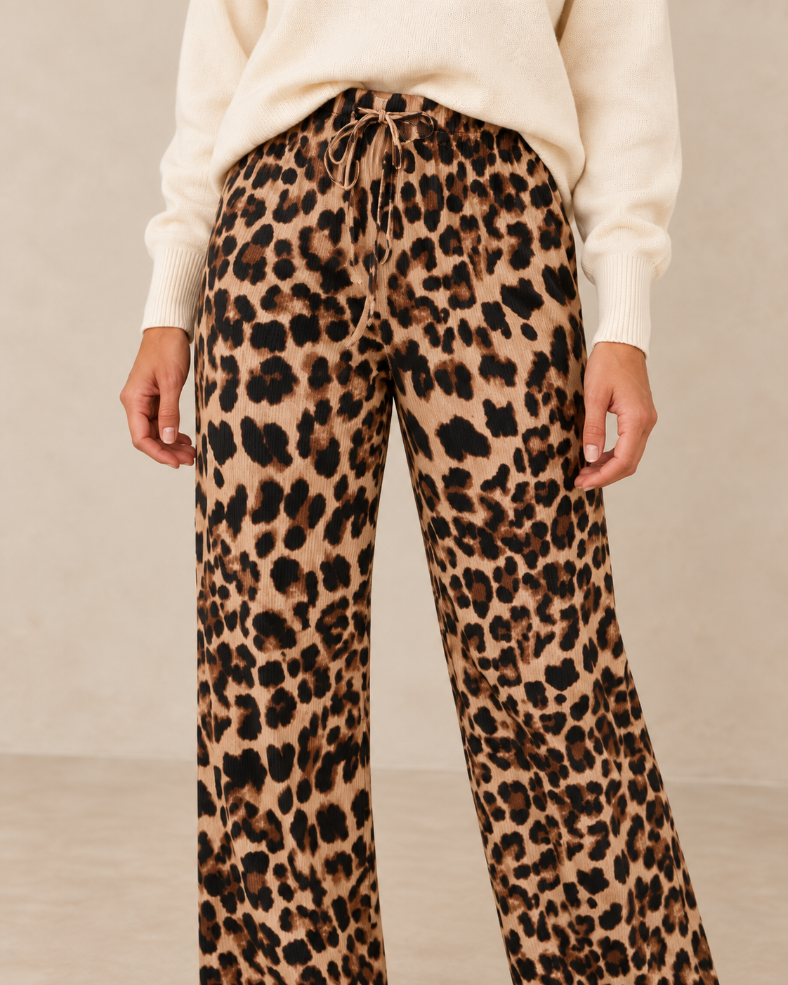 Gros plan du pantalon fluide léopard porté avec le pull écru sur fond beige